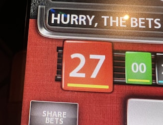 A digital display screen showing a casino betting interface, with text prompting to hurry bets and a highlighted number 27 in red. There are options for betting amounts and a 'share bets' button.
